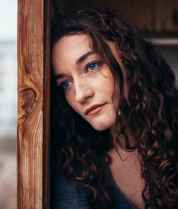 White woman leaning her head on a doorframe looking into the distance