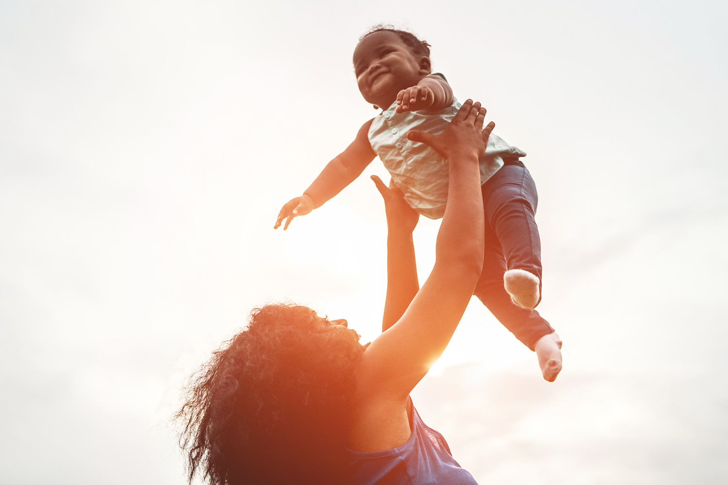 Woman Playing With A Happy Baby Outdoors, Holding The Baby High Up