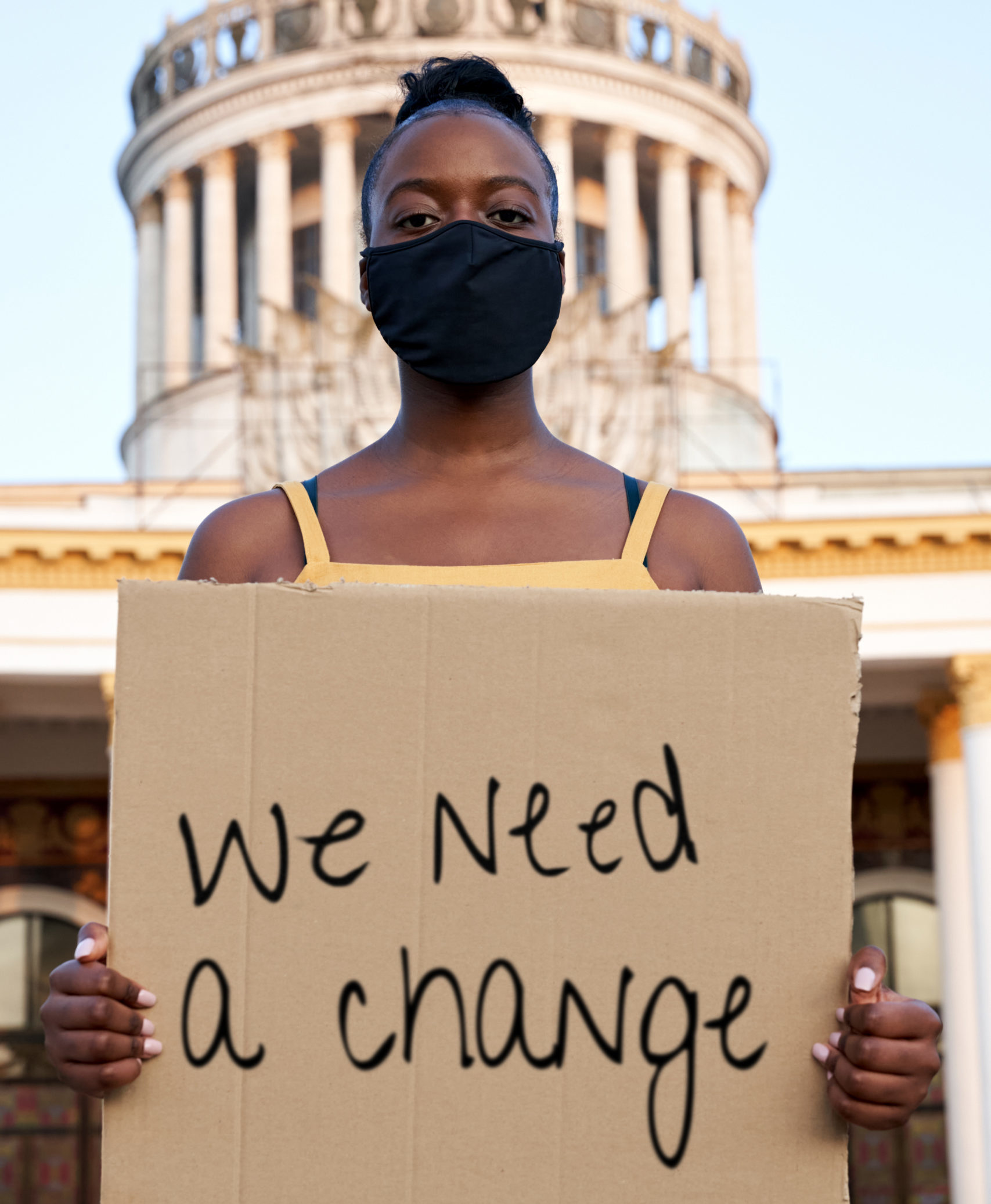 Black Woman Wearing Mouth Mask Holding A Placard Saying We Need A Change