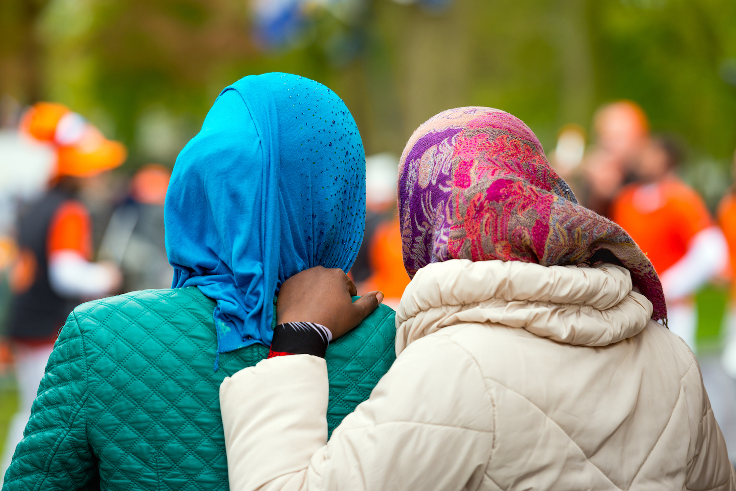 Two Women Wearing Colourful Scarves Photographed From The Back.