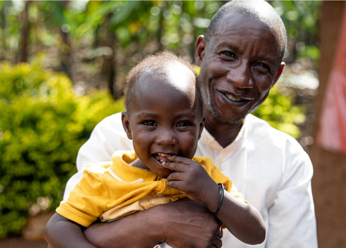 A Black Father Carries His Son, And Both Of Them Are Smiling.