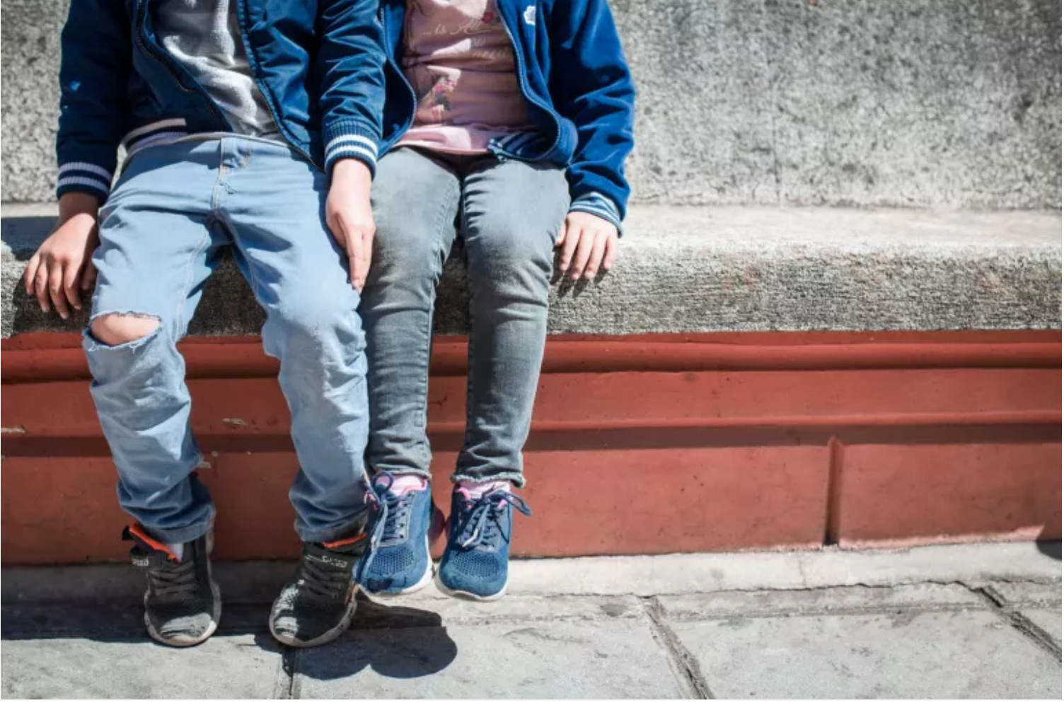 Picture Of Lower Half Of Two Young Children. They're Sitting On Concrete.