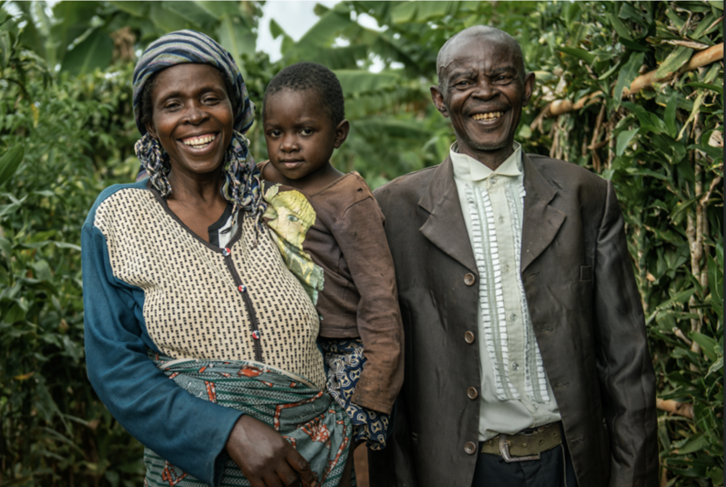 A Black Couple Standing, And The Woman Carrying Her Son. They Are Laughing And Facing The Camera.