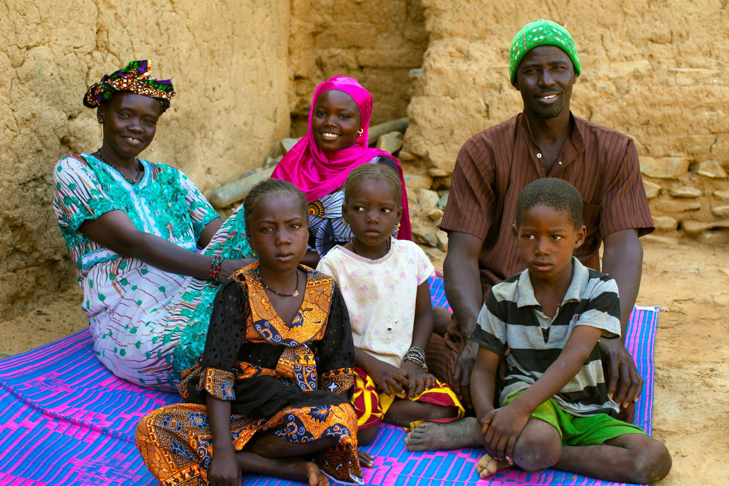 A Black Family All Sat On A Mat. They Are Smiling And Looking At The Camera.