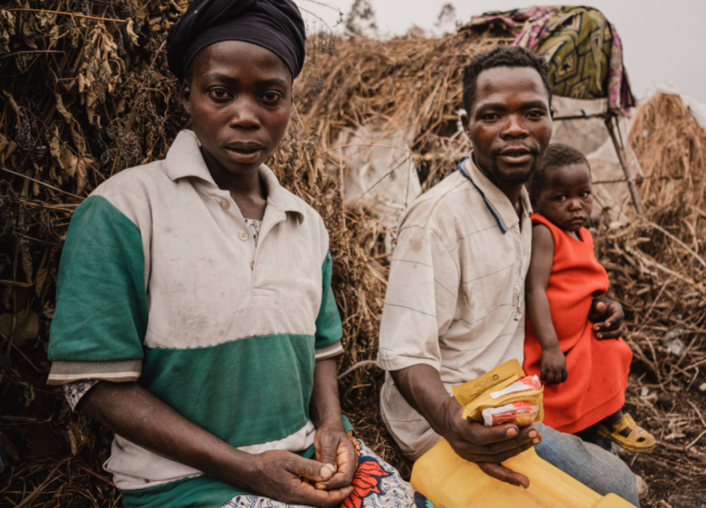 a black man and a black woman sitting side by side. The man is holding a small black child in an orange dress.
