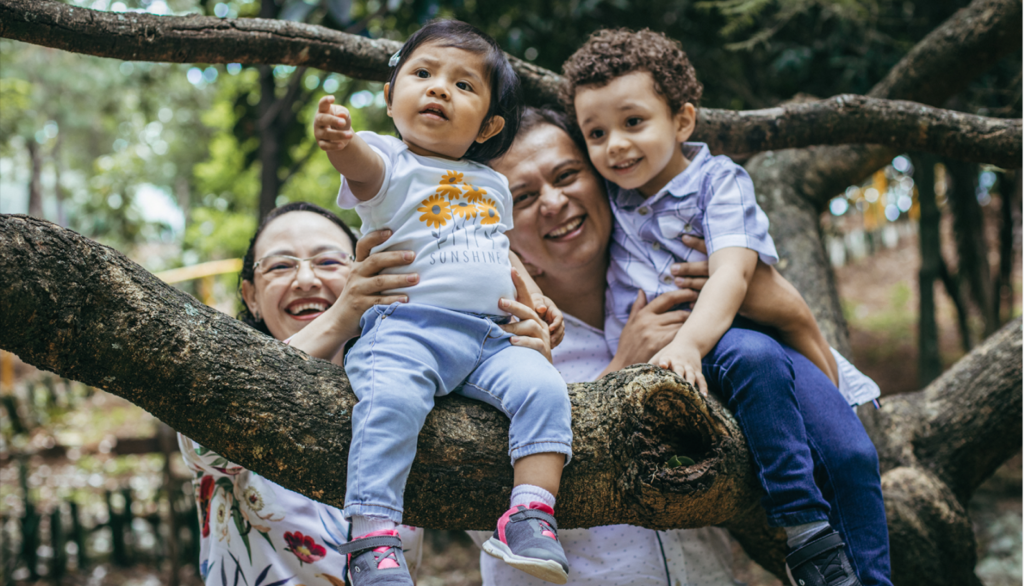 two Asian parents holding two Asian toddlers up on a tree. they're all smiling.
